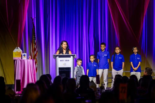 Mother speaking at podium with children on stage at ACE Scholarships fundraising luncheon Denver