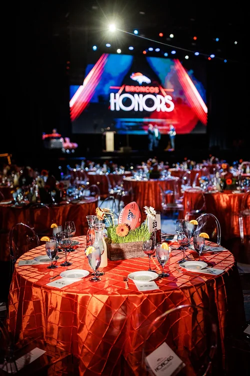 Denver Broncos Honors Awards setup with orange-draped tables and Honors stage screen at Mission Ballroom Denver